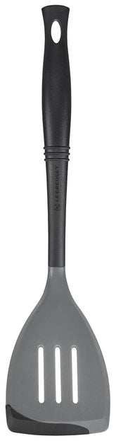 Le Creuset Revolution bi-material slotted spatula head angled for precise stirring on nonstick pans.