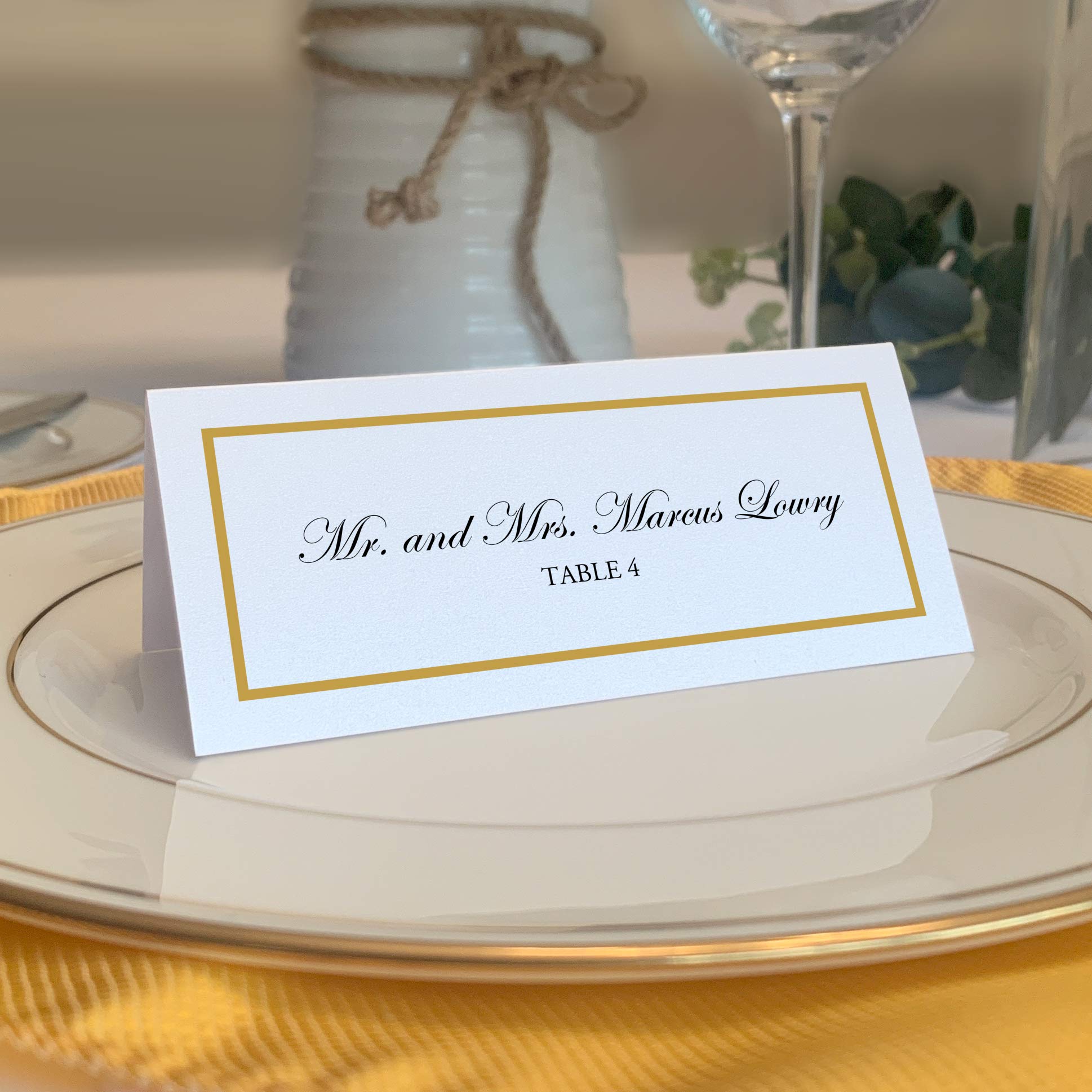Documents and Designs gold border place card on white table for an elegant wedding.
