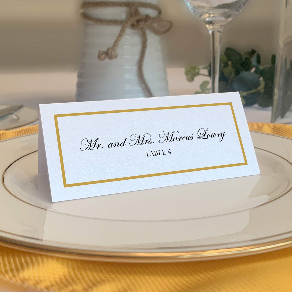 Documents and Designs gold border place card on white table for an elegant wedding.