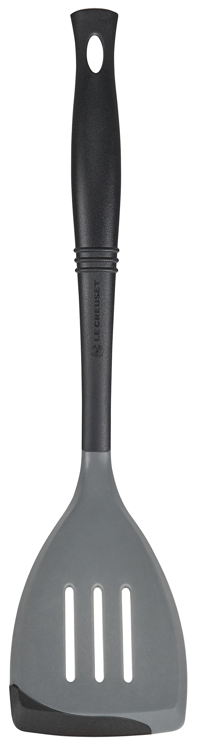 Le Creuset Revolution bi-material slotted spatula head angled for precise stirring on nonstick pans.