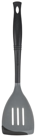 Le Creuset Revolution bi-material slotted spatula head angled for precise stirring on nonstick pans.