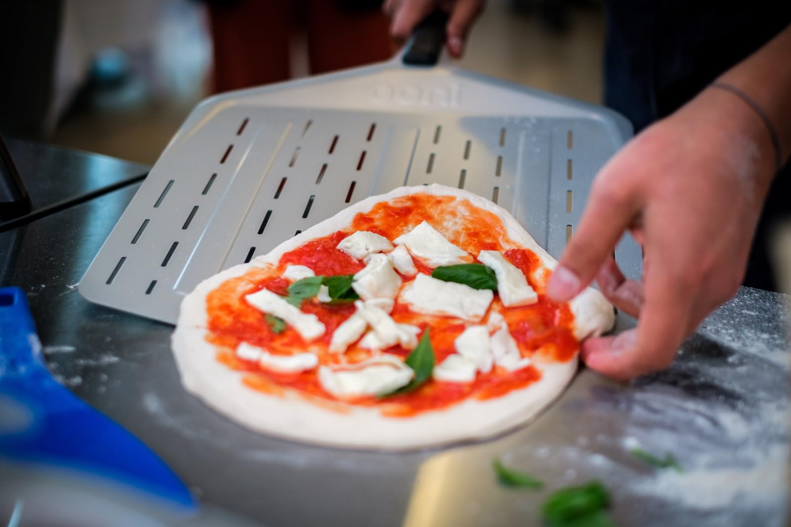 Ooni pizza peel lifts a pizza from a hot outdoor oven with control