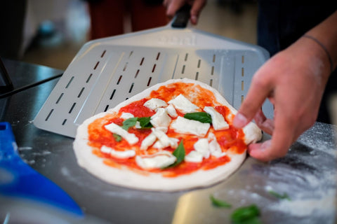 Ooni pizza peel lifts a pizza from a hot outdoor oven with control